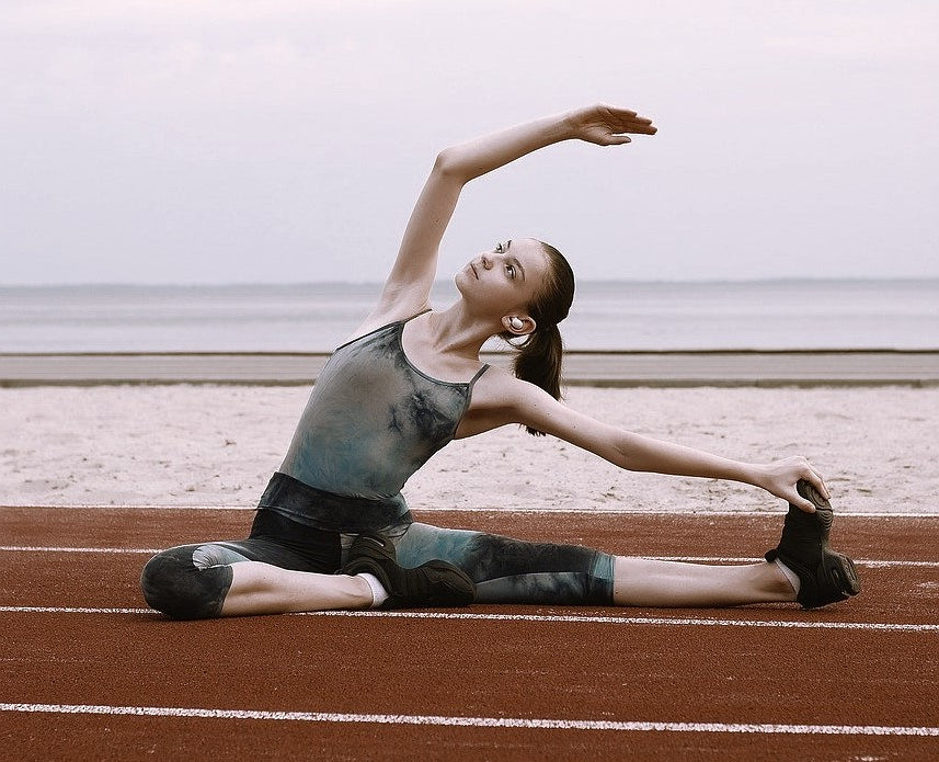 a woman wearing activewear made from synthetic fibers such as spandex is stretching on a racetrack before her run