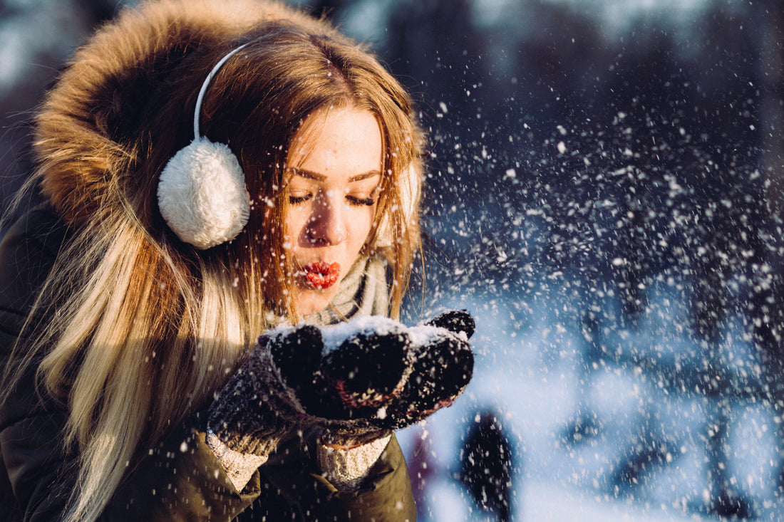 woman blowing at snowflakes to escape the winter blues. 