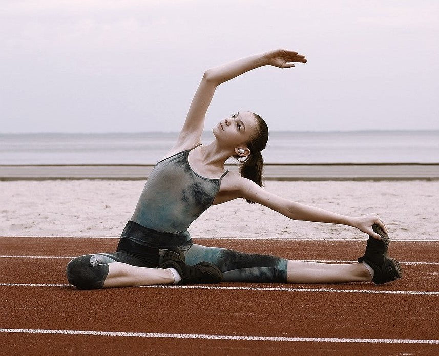 a woman wearing activewear made from synthetic fibers such as spandex is stretching on a racetrack before her run 