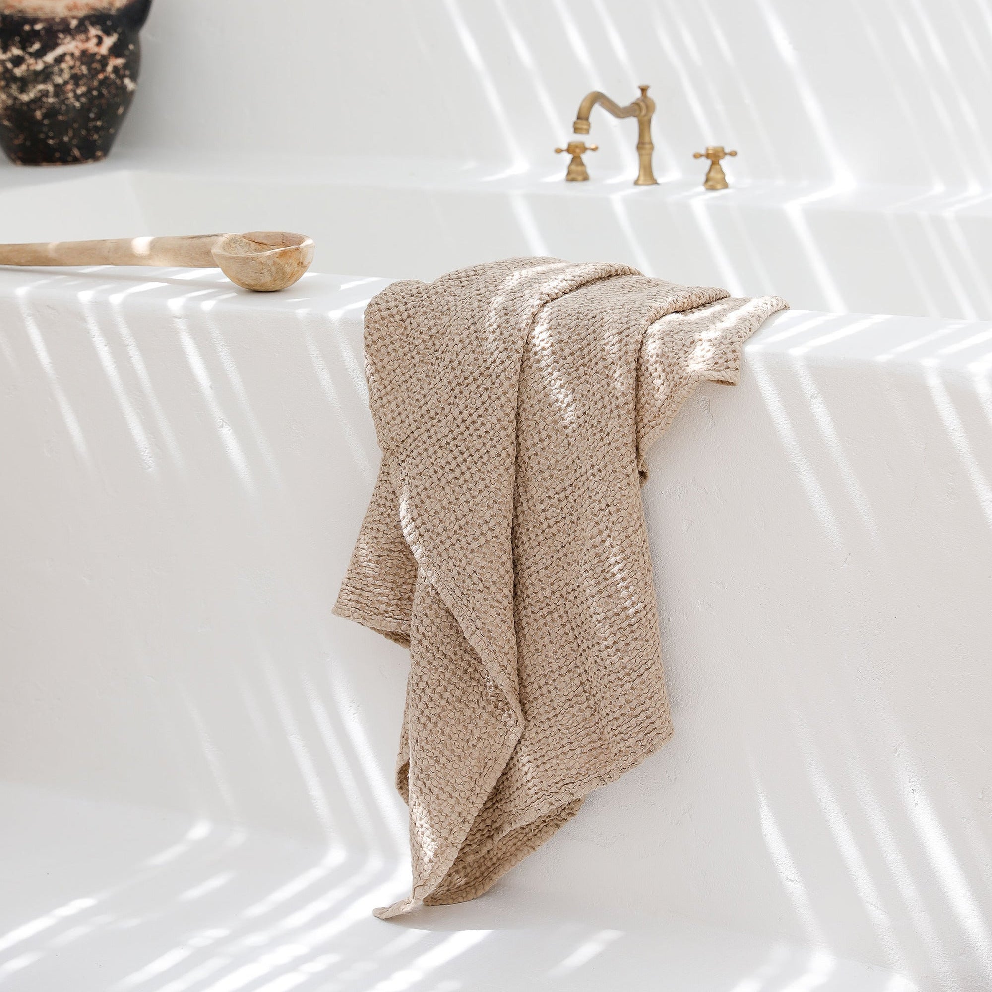 natural flax linen bath towel hanging on a white bath tub flooded by natural light
