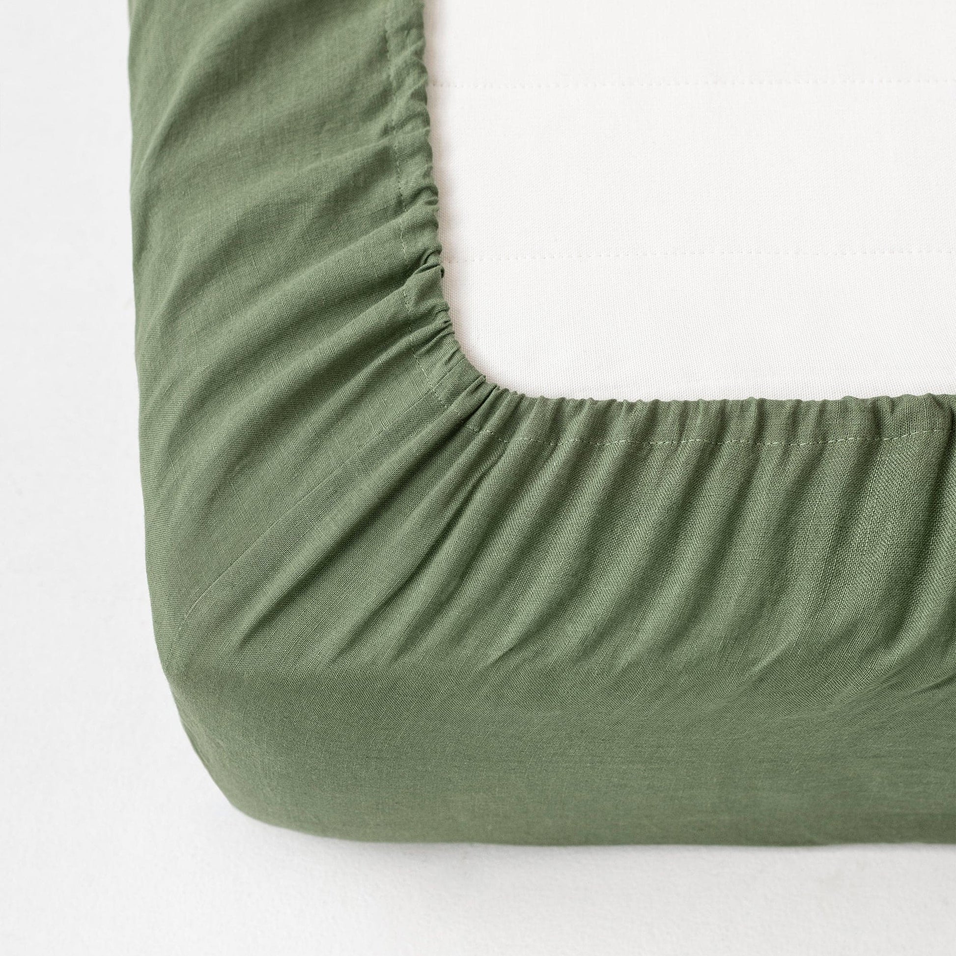 Green fitted sheet on a mattress corner with a white background