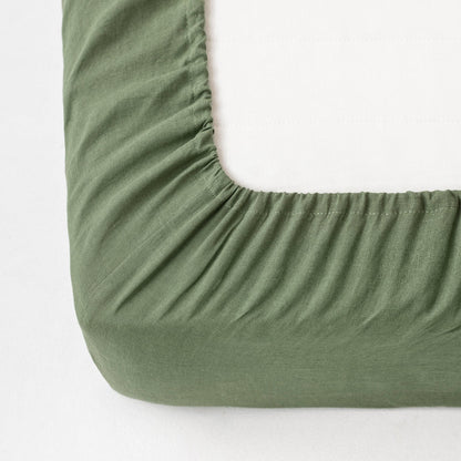 Green fitted sheet on a mattress corner with a white background