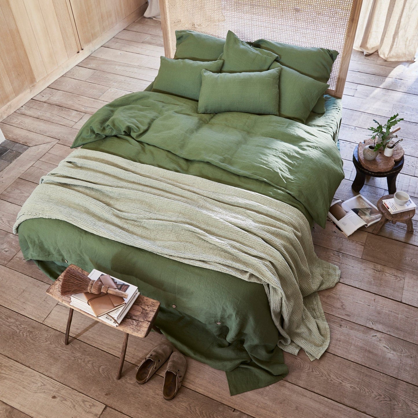 Green bedding set on a bed in a room with wooden flooring and decor.